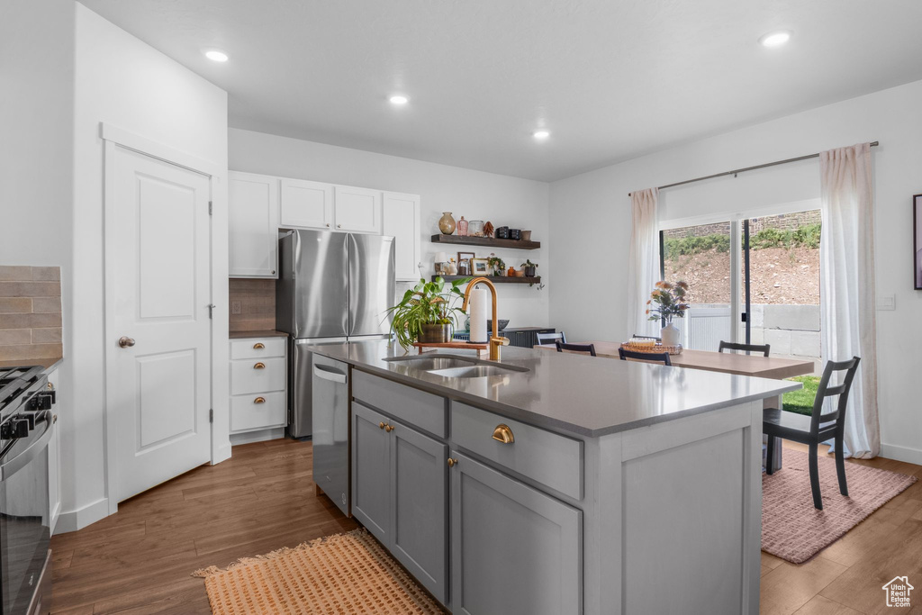 Kitchen with a sink, stainless steel appliances, wood finished floors, gray cabinets, and white cabinets