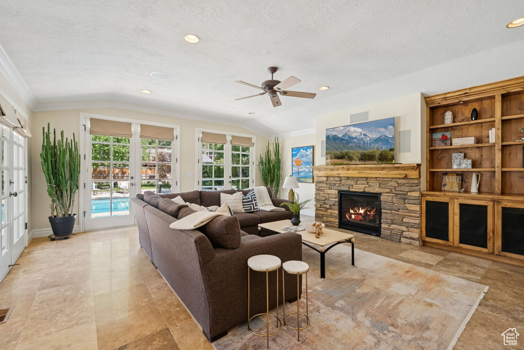 Living room with french doors, lofted ceiling, crown molding, a textured ceiling, and a fireplace