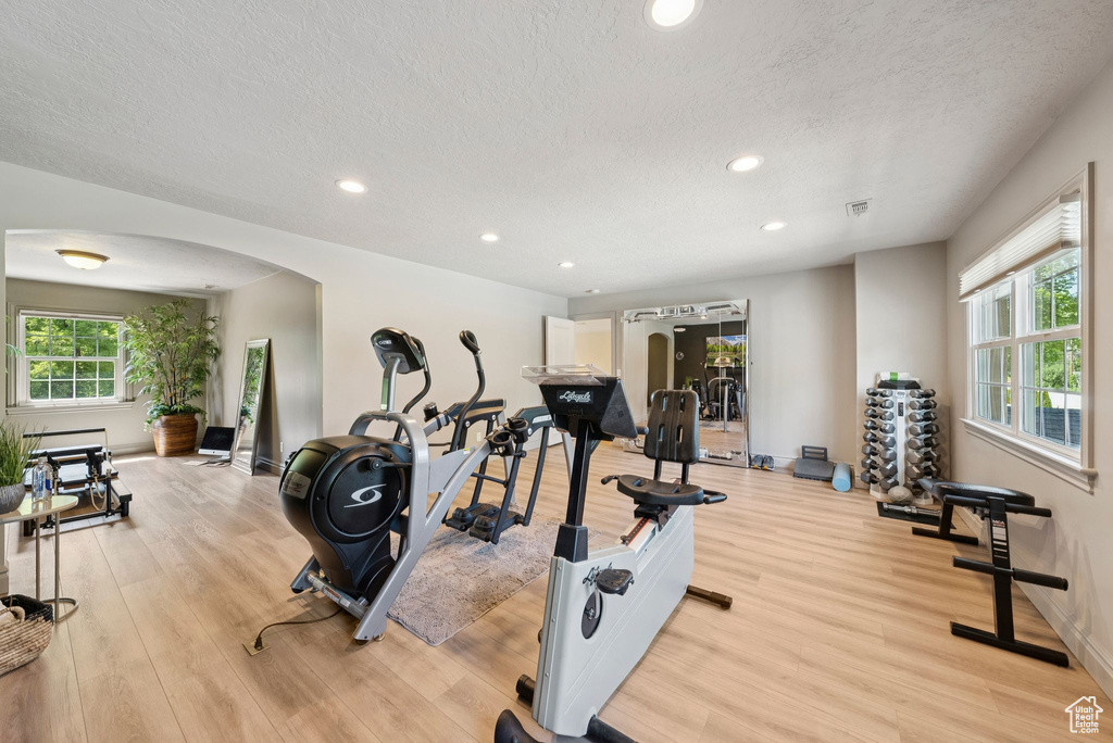 Workout area featuring arched walkways, light wood finished floors, a textured ceiling, recessed lighting, and baseboards