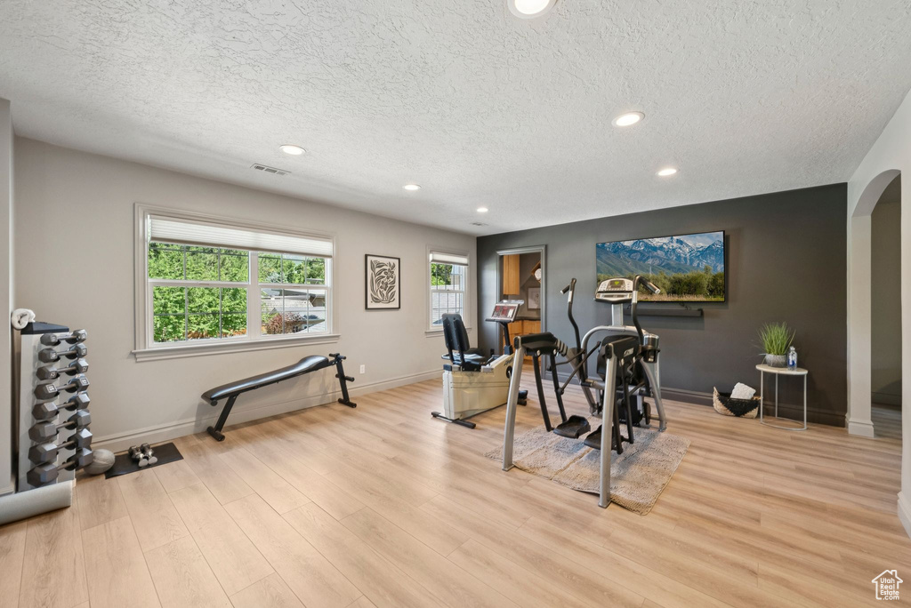 Workout area with a textured ceiling, arched walkways, recessed lighting, light wood-style floors, and baseboards