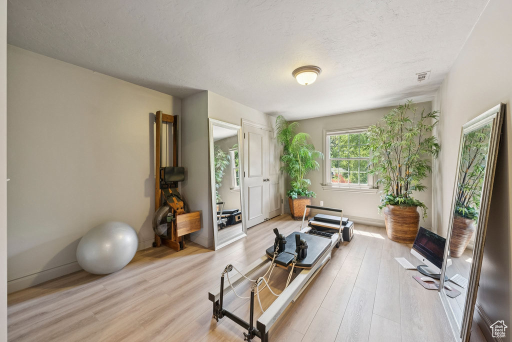 Workout room with a textured ceiling, light wood-style floors, and baseboards