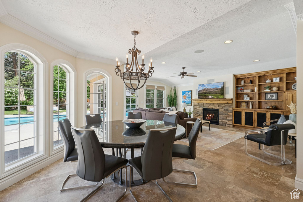 Dining room featuring a textured ceiling, plenty of natural light, ornamental molding, a stone fireplace, and a chandelier