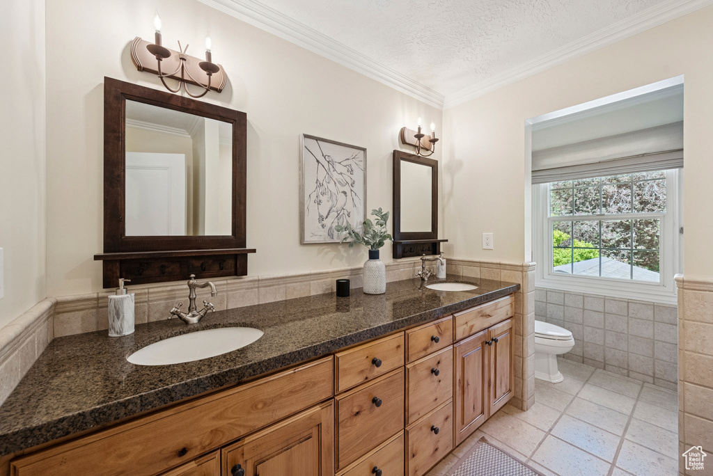 Bathroom with tile walls, tile patterned flooring, double vanity, toilet, and a wainscoted wall