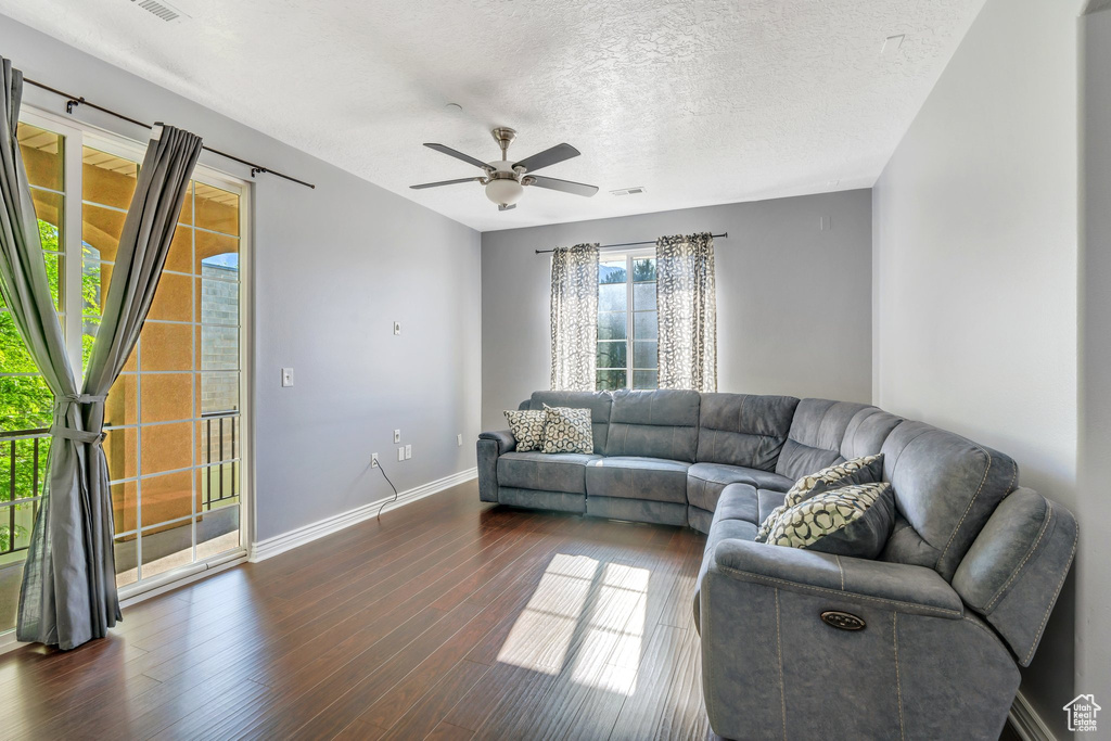 Living area with ceiling fan, dark wood-style flooring, baseboards, and a textured ceiling