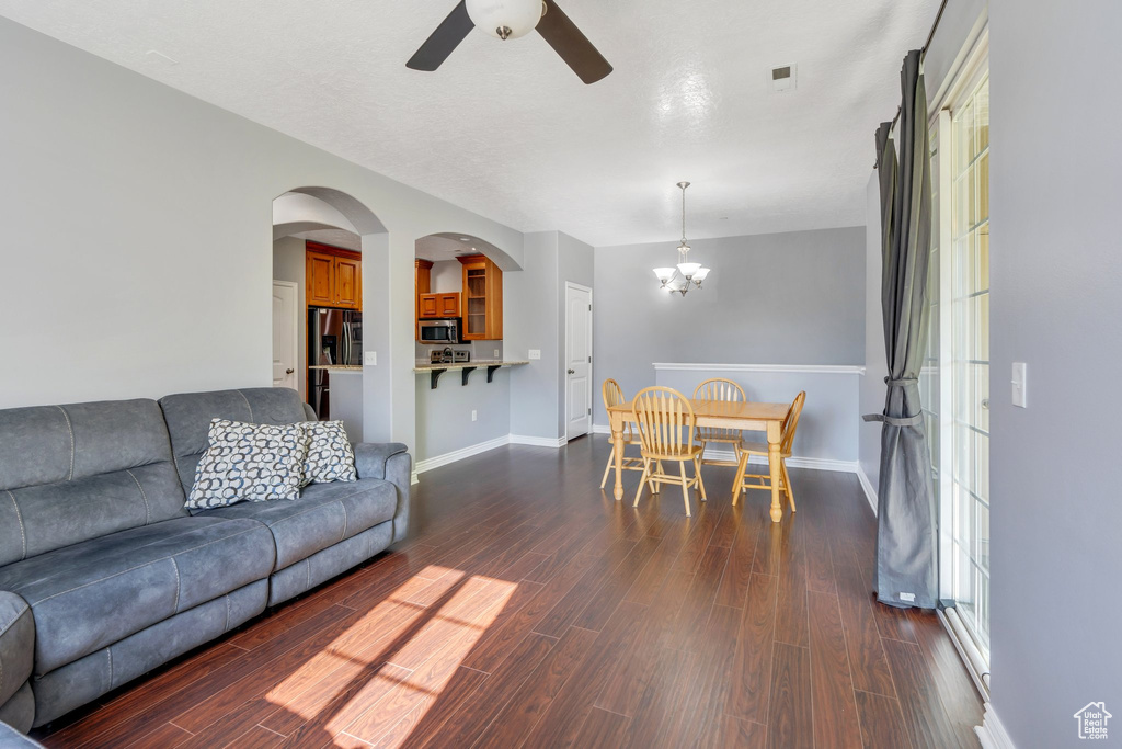 Living room featuring a chandelier, a ceiling fan, dark wood-style flooring, and baseboards