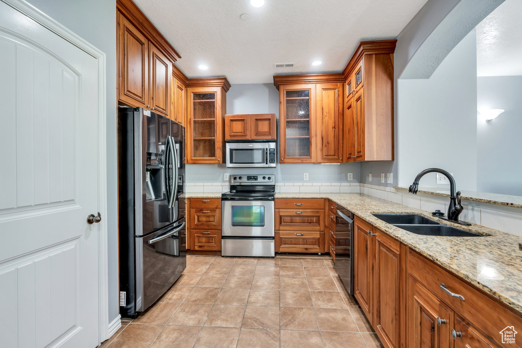 Kitchen featuring appliances with stainless steel finishes, a sink, brown cabinets, light stone countertops, and recessed lighting