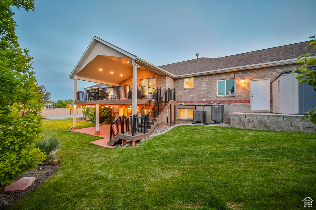 Back of property featuring stairway, a deck, brick siding, a lawn, and central air condition unit