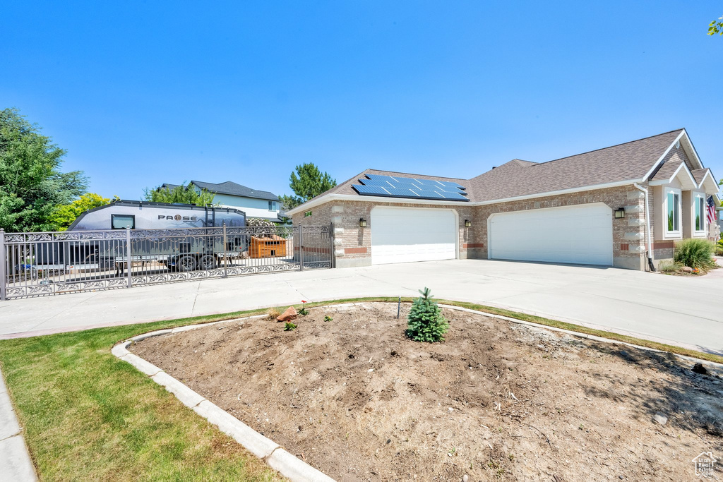 View of front of property featuring brick siding, solar panels, a garage, and concrete driveway
