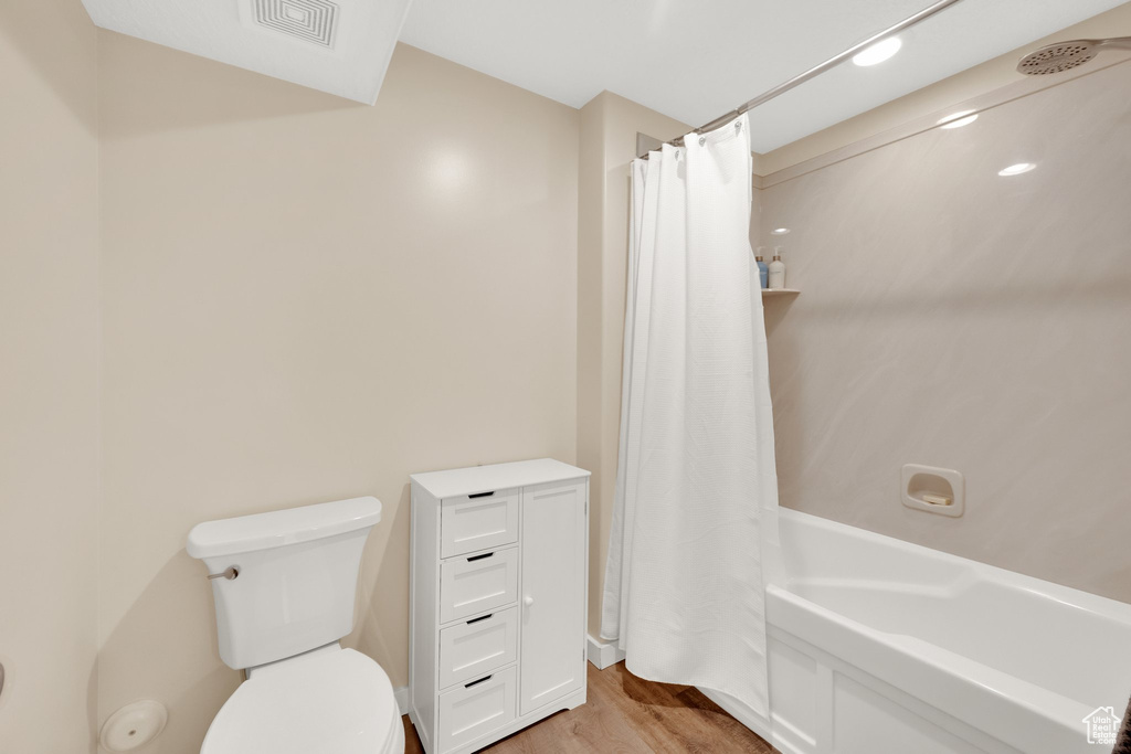 Full bath with wood finished floors, toilet, and shower / bath combo with shower curtain