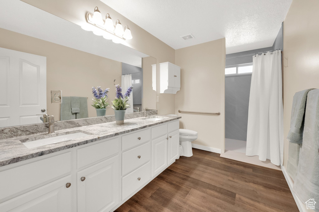 Full bathroom featuring toilet, double vanity, a shower with shower curtain, wood finished floors, and baseboards