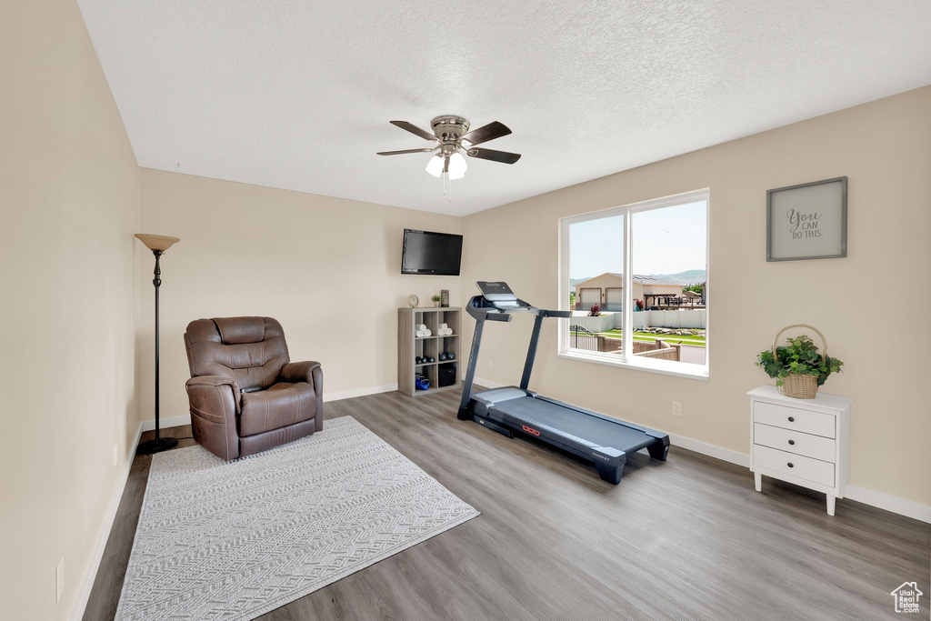 Exercise area with wood finished floors, a ceiling fan, baseboards, and a textured ceiling