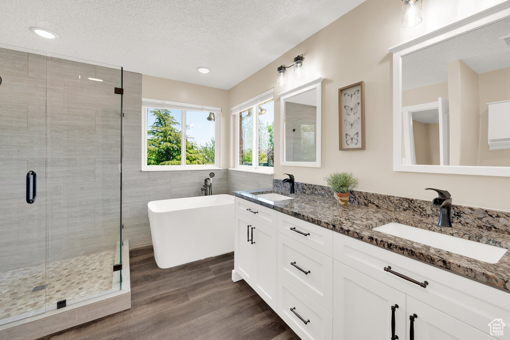 Full bath featuring a stall shower, a textured ceiling, double vanity, wood finished floors, and a soaking tub