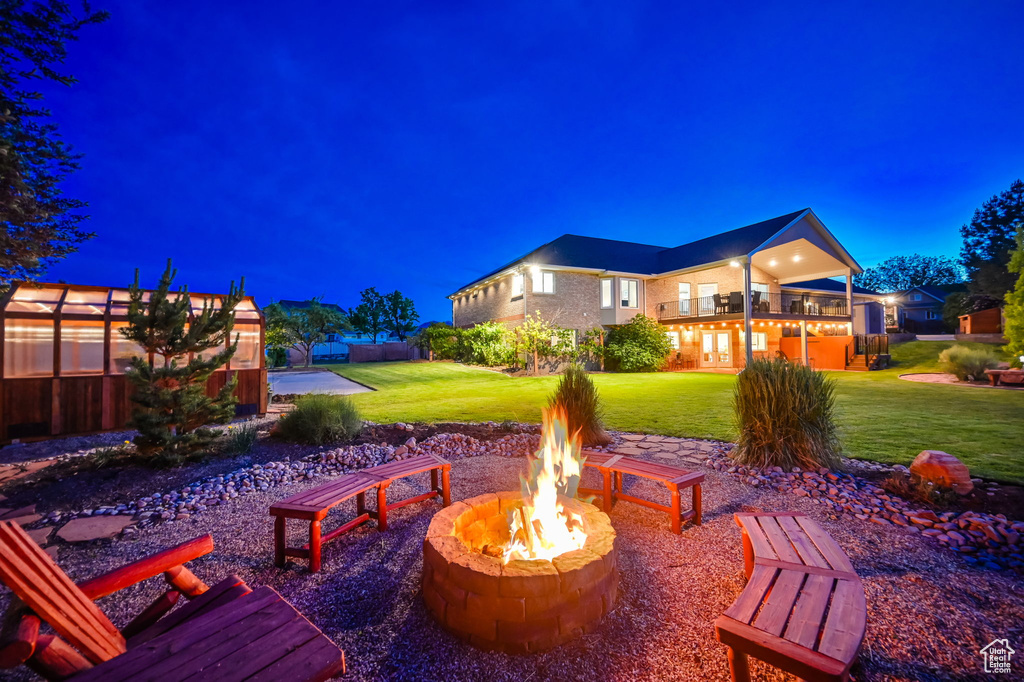 Patio at night featuring a fire pit, a yard, and a balcony