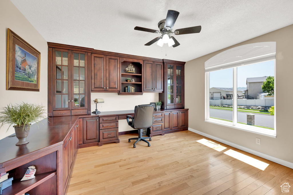 Home office with built in desk, a ceiling fan, light wood finished floors, baseboards, and a textured ceiling