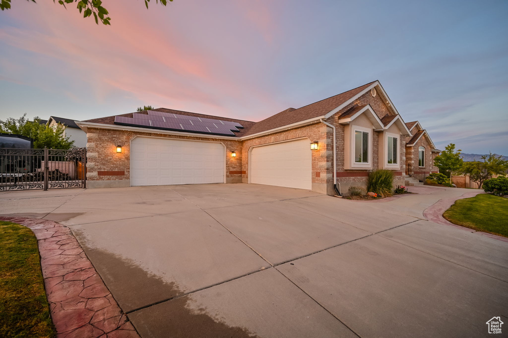 Ranch-style house featuring driveway, a garage, brick siding, solar panels, and a shingled roof
