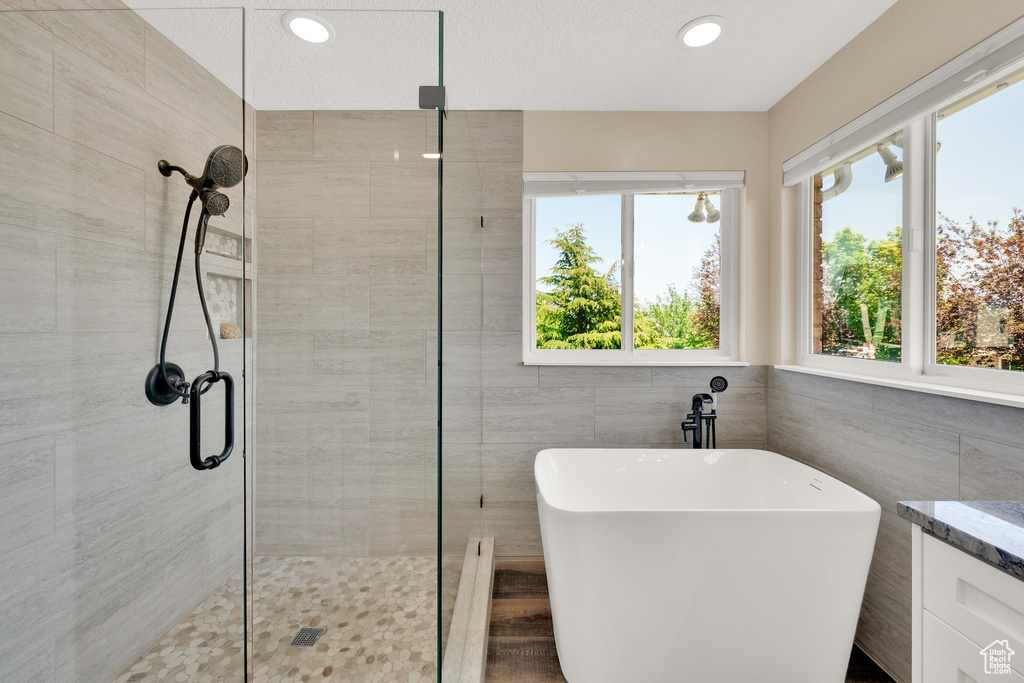 Bathroom featuring a shower stall, a soaking tub, tile walls, recessed lighting, and vanity