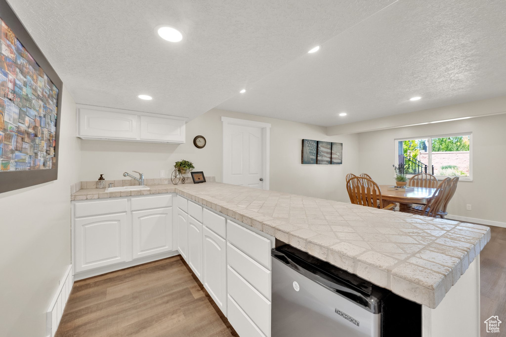 Kitchen featuring a peninsula, light wood-style flooring, a sink, a textured ceiling, and recessed lighting
