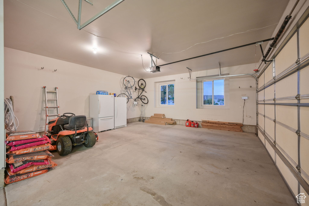 Garage with freestanding refrigerator, refrigerator, and a garage door opener