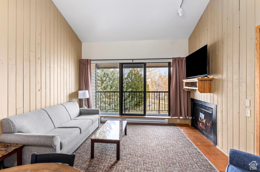 Living room featuring wood walls, a glass covered fireplace, and a baseboard heating unit