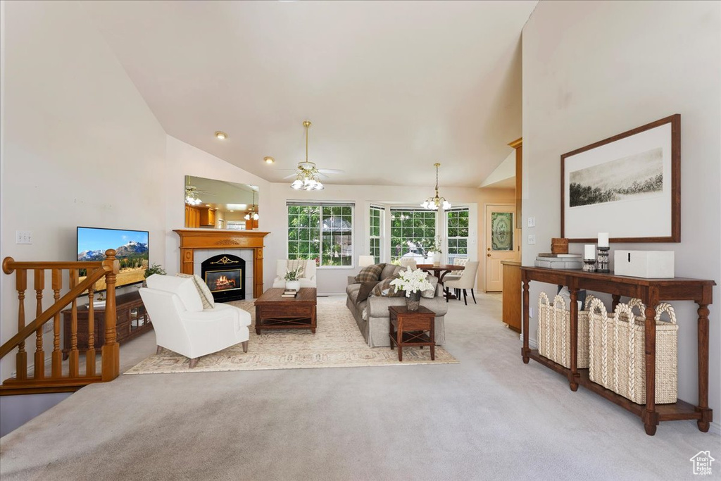 Living room featuring light colored carpet, a tile fireplace, ceiling fan, high vaulted ceiling, and a chandelier