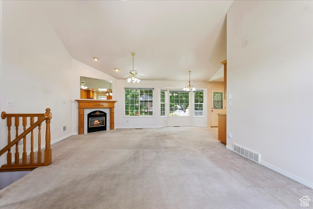 Unfurnished living room featuring a tiled fireplace, baseboards, light colored carpet, a ceiling fan, and high vaulted ceiling