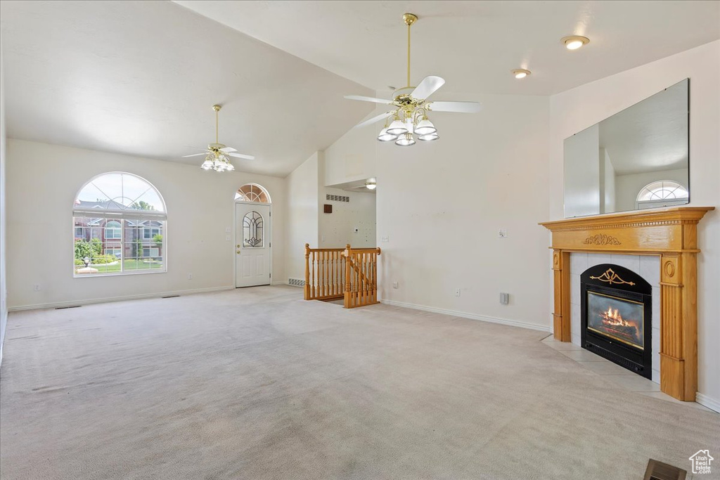 Unfurnished living room featuring ceiling fan, light carpet, a tile fireplace, high vaulted ceiling, and baseboards