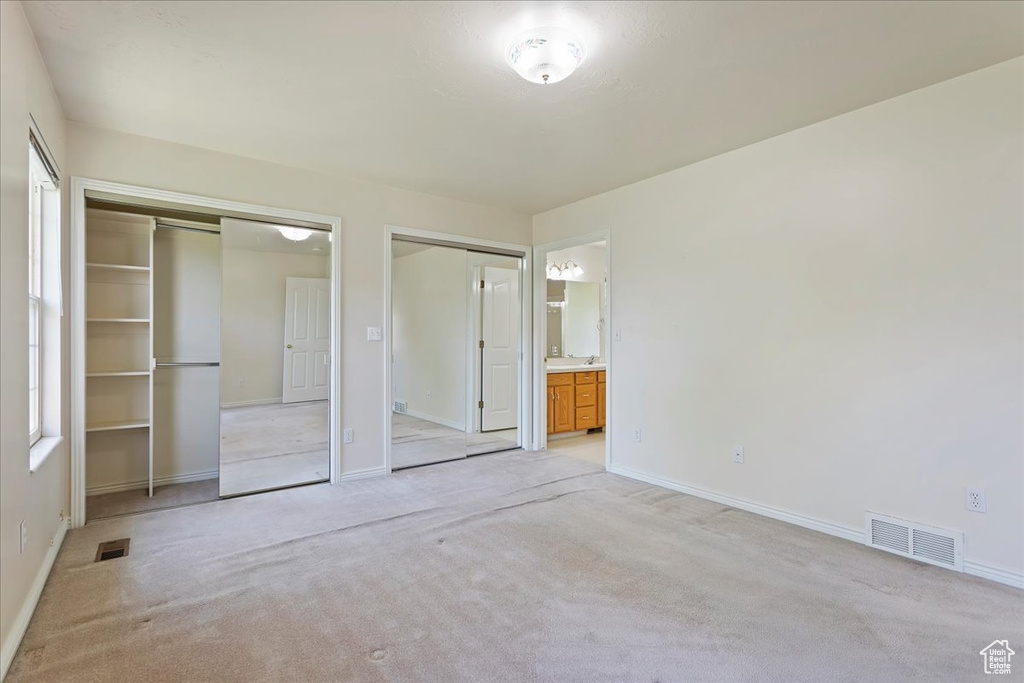 Unfurnished bedroom featuring two closets, baseboards, and light carpet