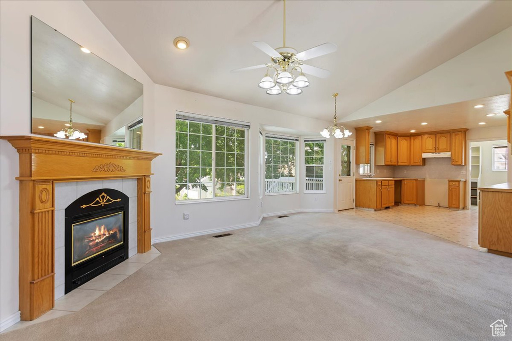 Unfurnished living room featuring vaulted ceiling, a chandelier, light carpet, a tile fireplace, and a ceiling fan