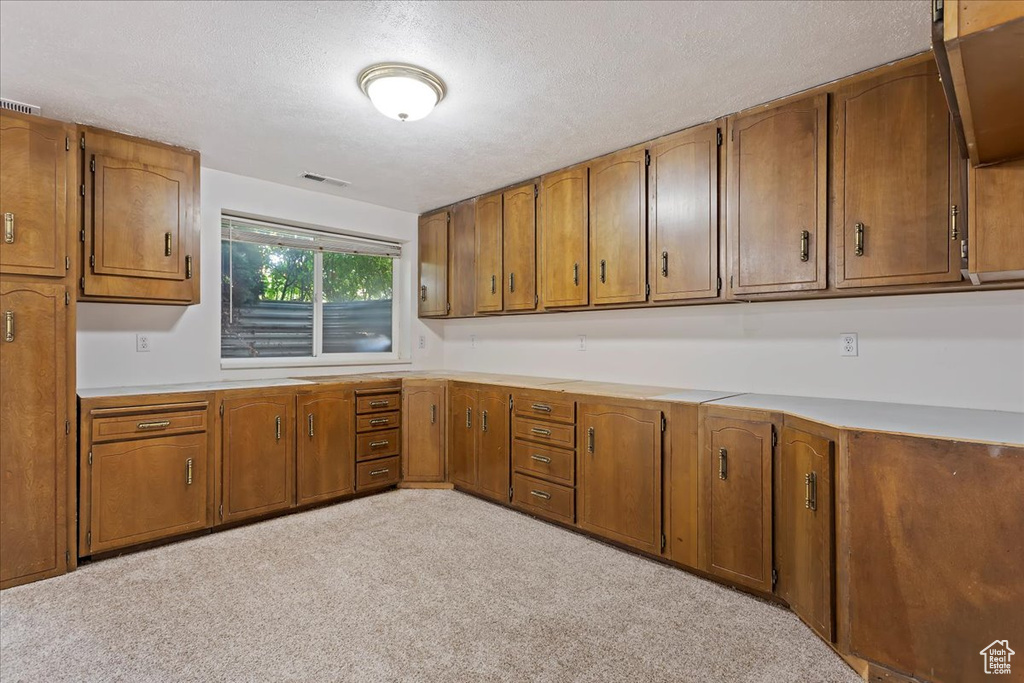 Kitchen featuring brown cabinets, light countertops, a textured ceiling, and carpet flooring