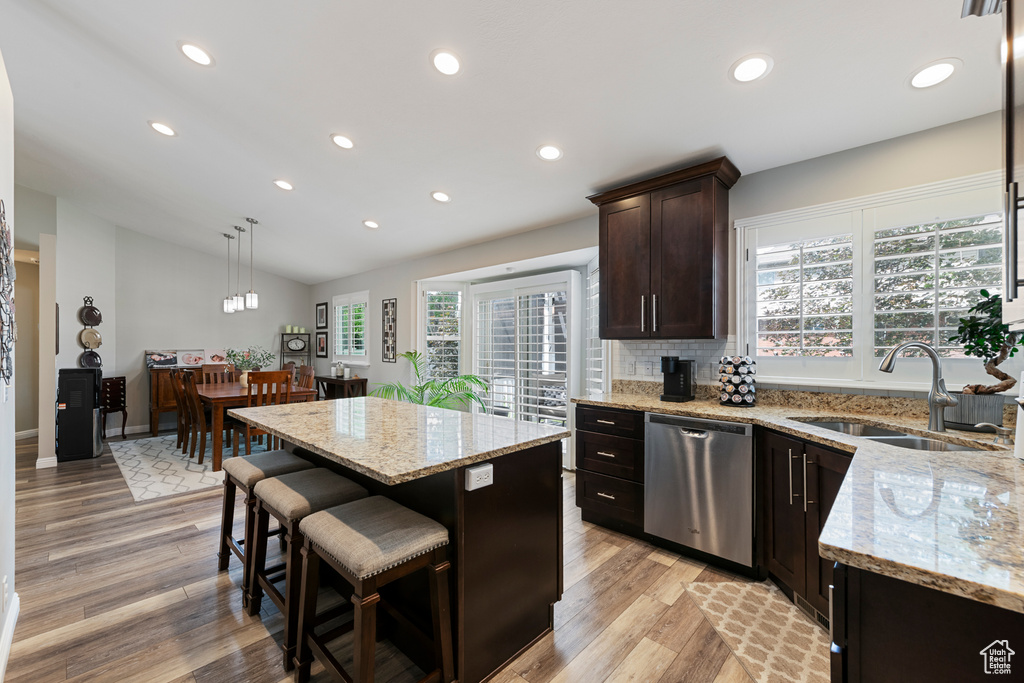 Kitchen with stainless steel dishwasher, a sink, lofted ceiling, light wood-style floors, and light stone countertops
