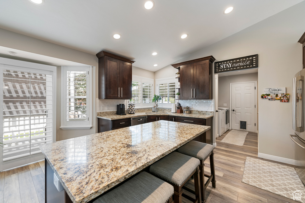 Kitchen with independent washer and dryer, dark brown cabinetry, dishwasher, backsplash, and light stone counters