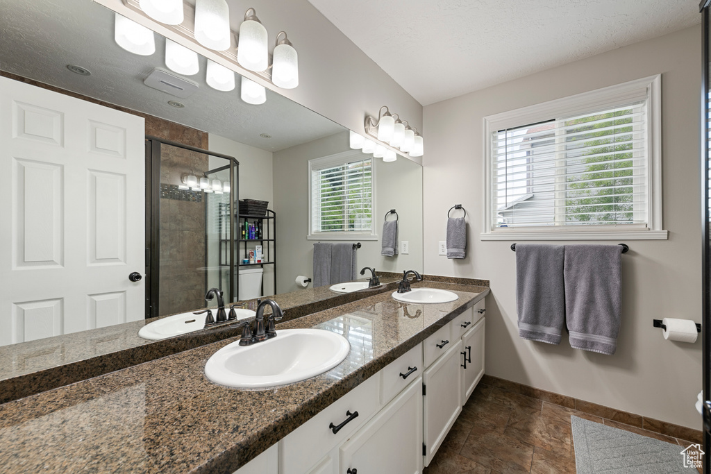 Full bath with baseboards, double vanity, and a stall shower
