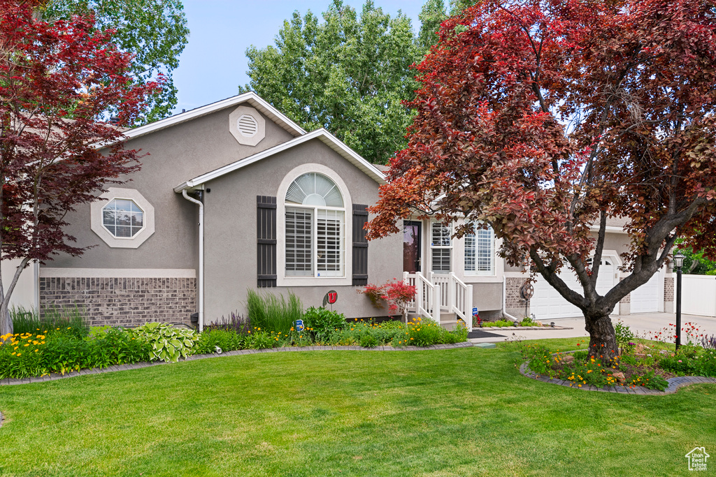 View of front facade featuring stucco siding, a front lawn, driveway, and an attached garage