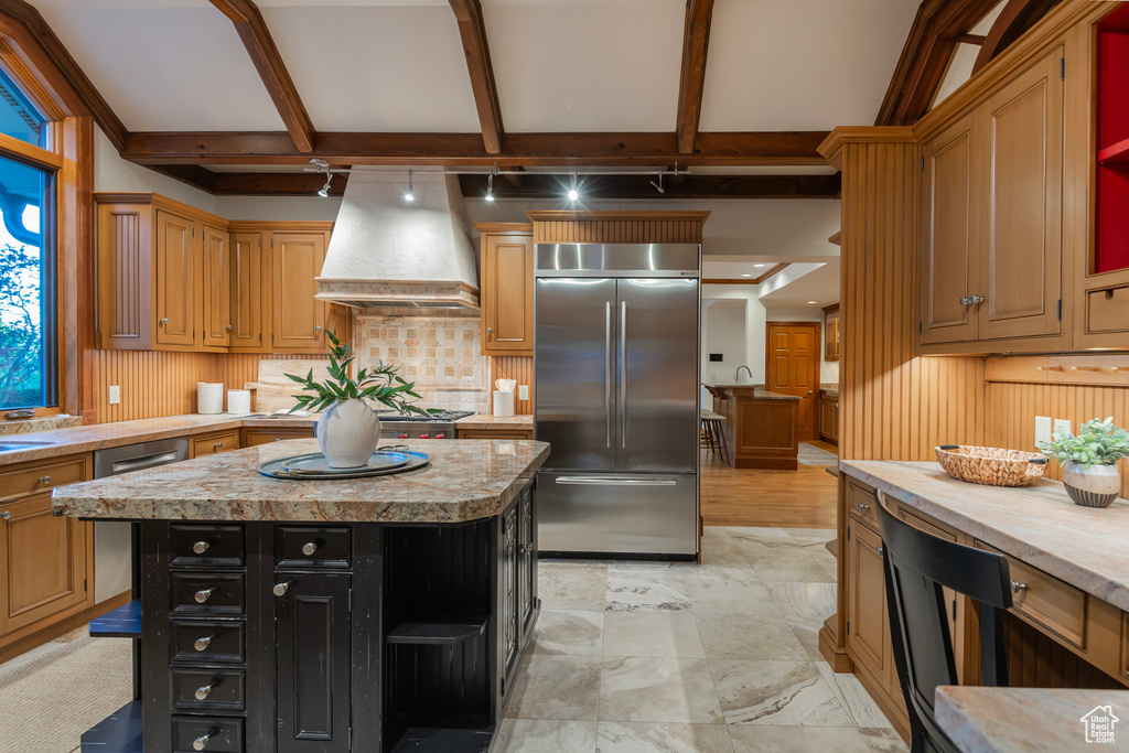 Kitchen with stainless steel built in fridge, wall chimney exhaust hood, decorative backsplash, light countertops, and a kitchen island