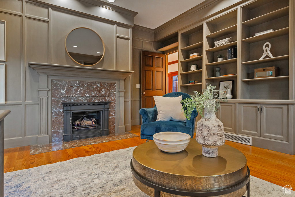 Living area featuring light wood-style floors, crown molding, a decorative wall, and a high end fireplace