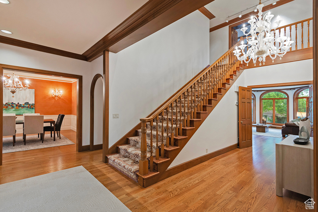 Staircase featuring a chandelier, wood finished floors, baseboards, crown molding, and rail lighting