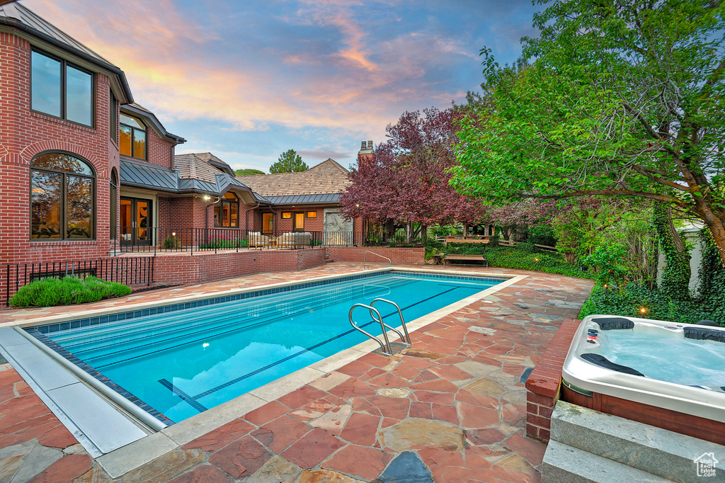 Pool at dusk featuring a hot tub and a patio