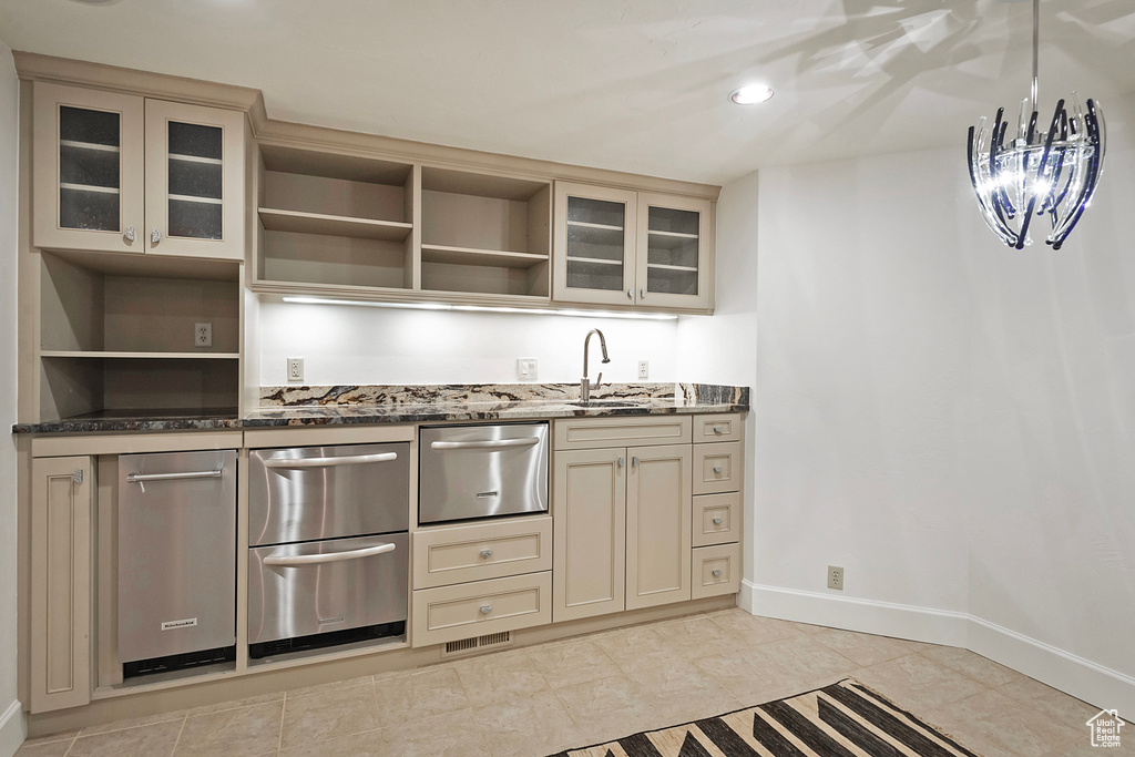 Kitchen featuring open shelves, dishwasher, a sink, dark stone counters, and cream cabinets