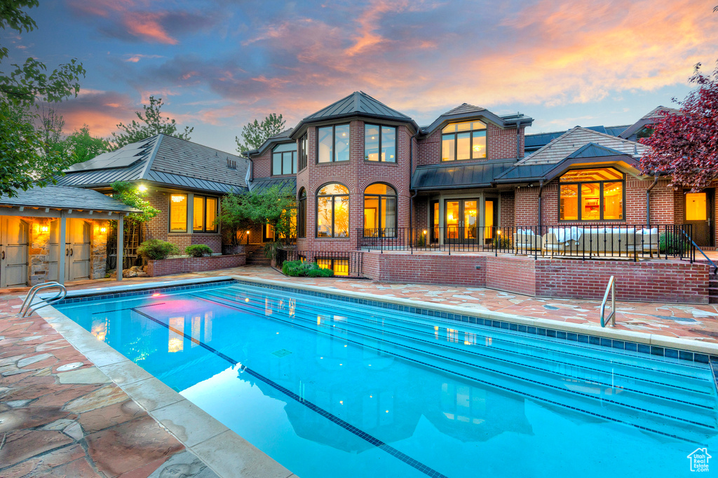 Back of property at dusk featuring brick siding, an outdoor pool, and a patio