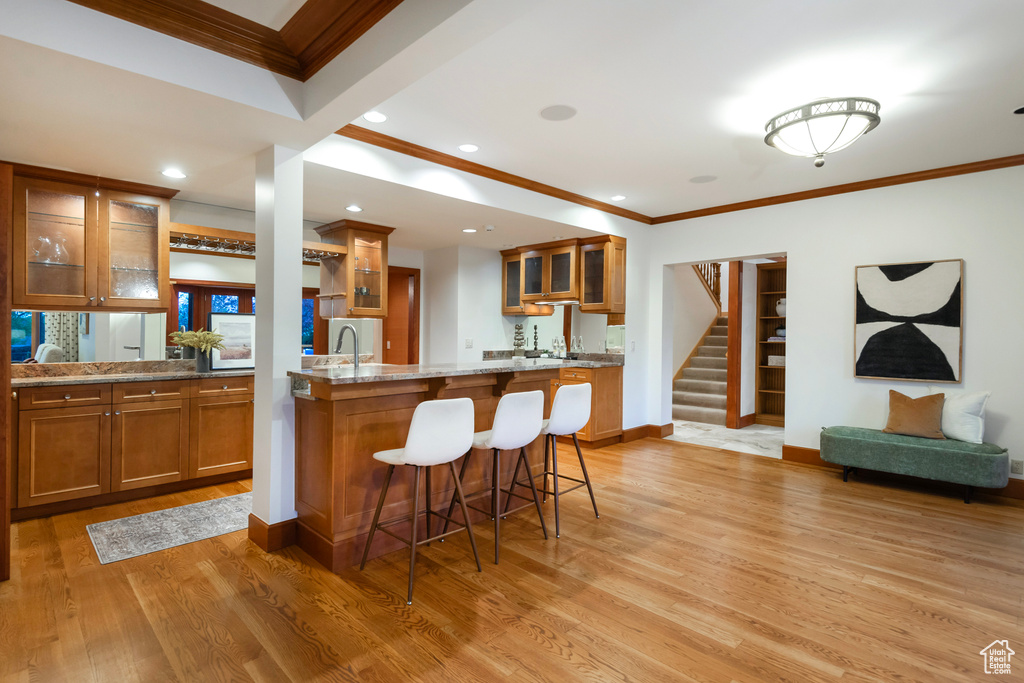 Kitchen featuring crown molding, brown cabinets, a kitchen bar, light wood-style floors, and recessed lighting