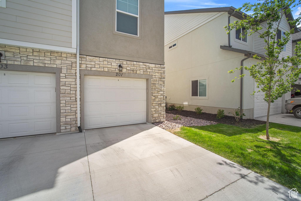 View of property exterior featuring stone siding, a garage, stucco siding, and concrete driveway