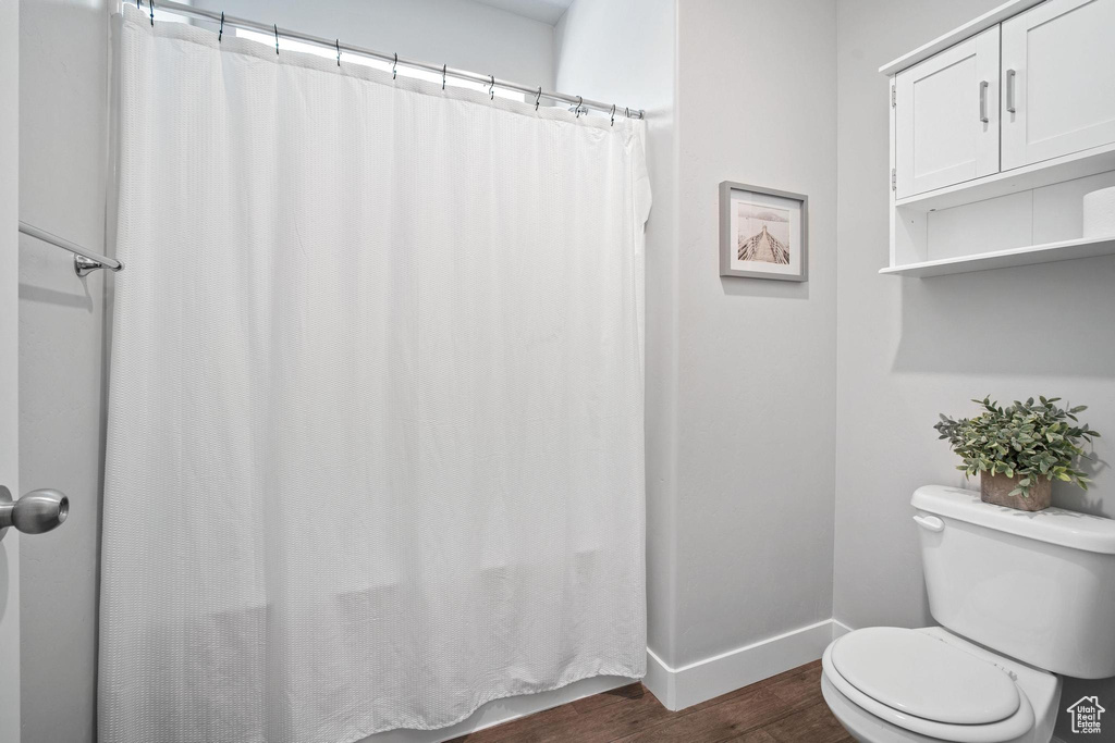 Full bath with wood finished floors, toilet, baseboards, and curtained shower