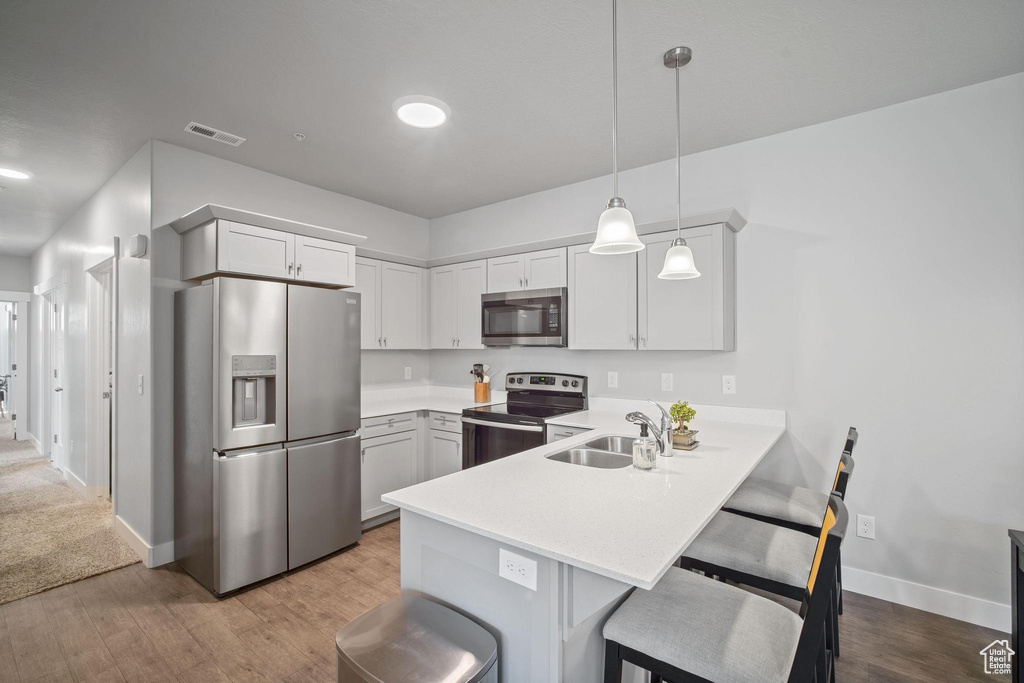 Kitchen with stainless steel appliances, a sink, a peninsula, a breakfast bar, and light countertops