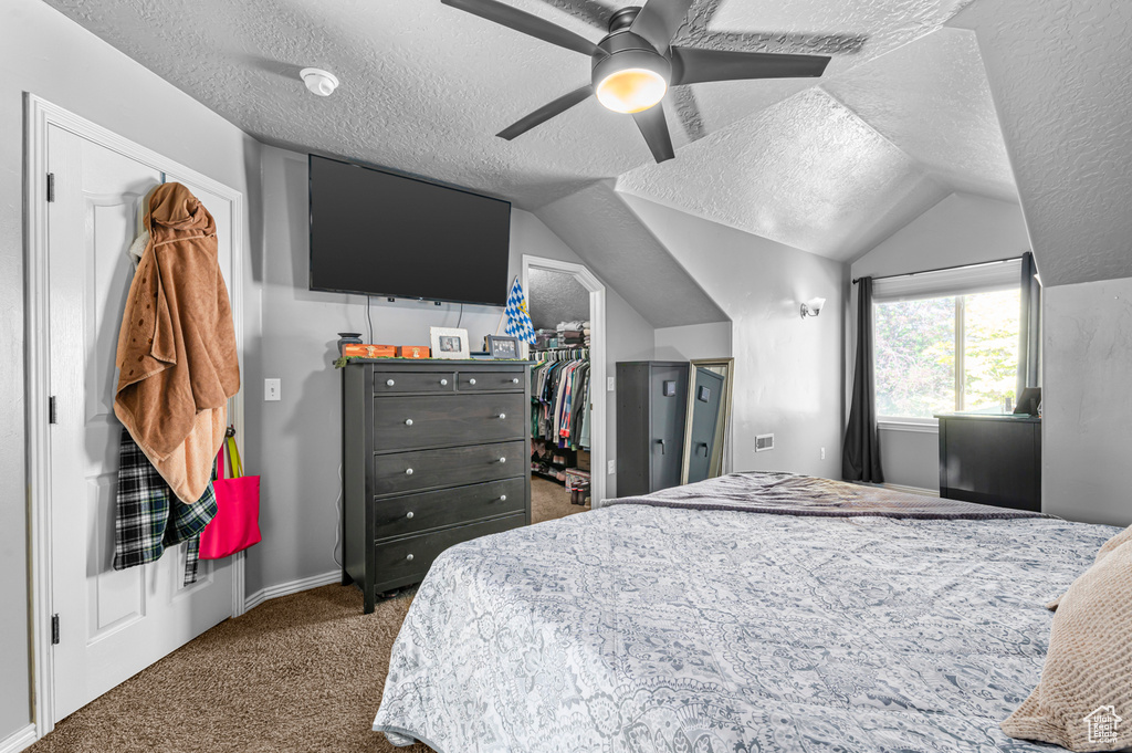 Bedroom featuring a textured ceiling, carpet flooring, a spacious closet, lofted ceiling, and ceiling fan