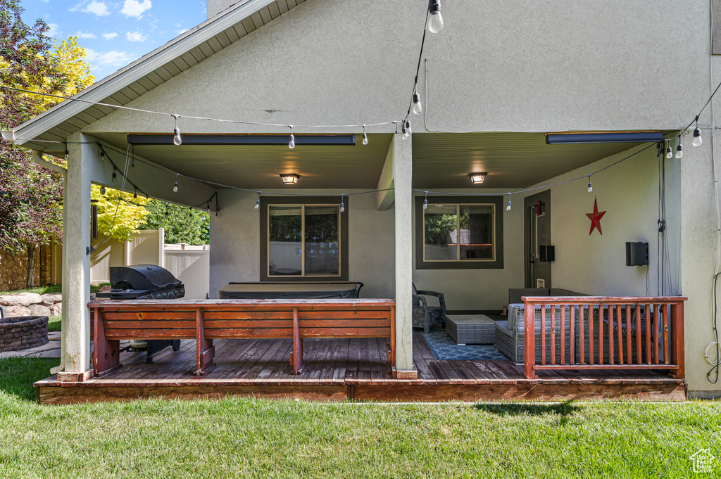 Rear view of property featuring a wooden deck, stucco siding, an outdoor hangout area, and a lawn