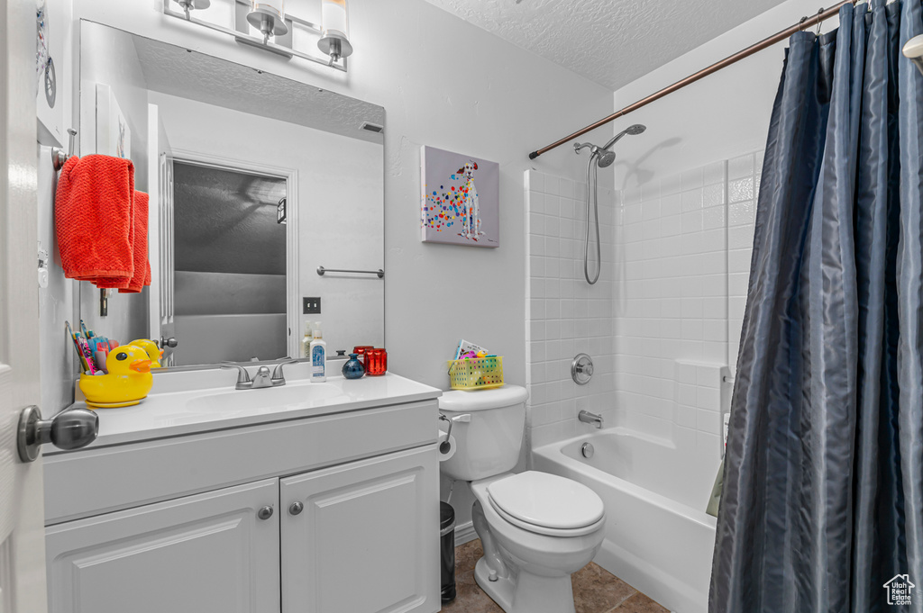 Bathroom with a textured ceiling, shower / tub combo, toilet, vanity, and tile patterned flooring