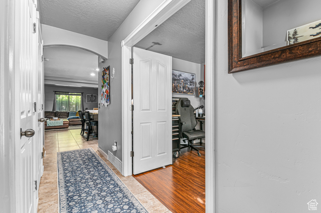 Corridor with a desk, arched walkways, tile patterned flooring, and a textured ceiling