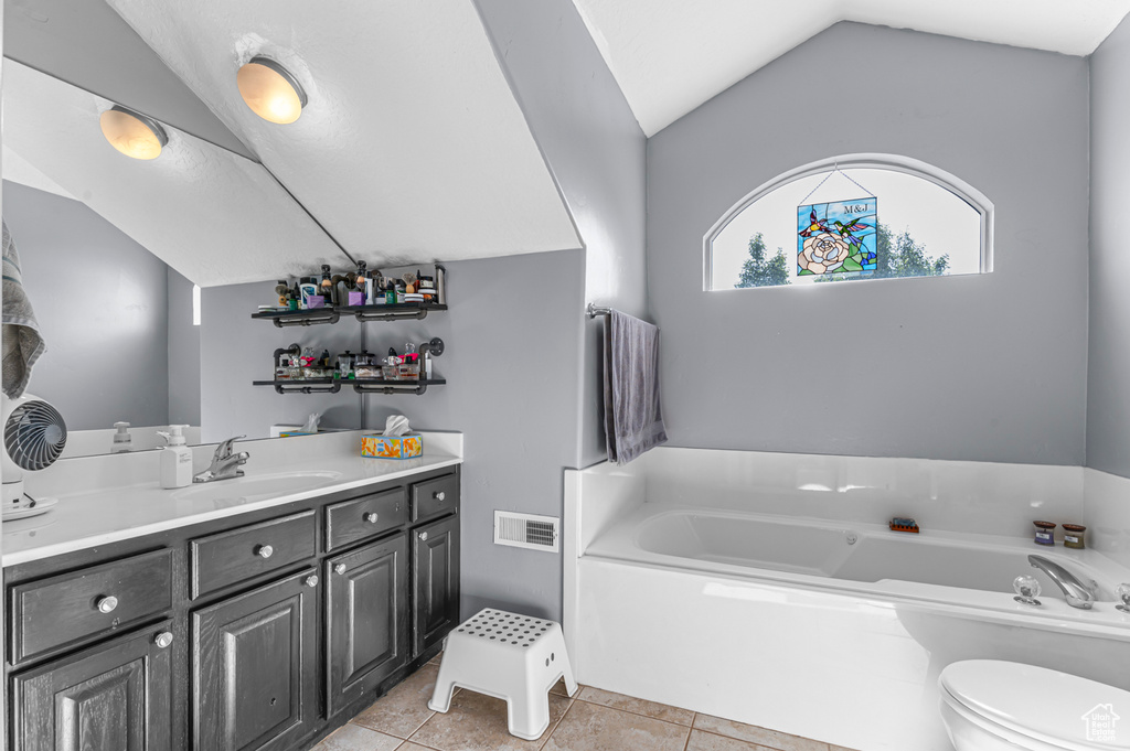 Full bath featuring vanity, lofted ceiling, a bath, toilet, and tile patterned floors