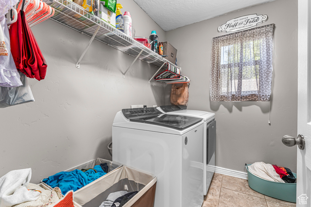 Laundry room with washer and dryer, light tile patterned flooring, baseboards, and a textured ceiling