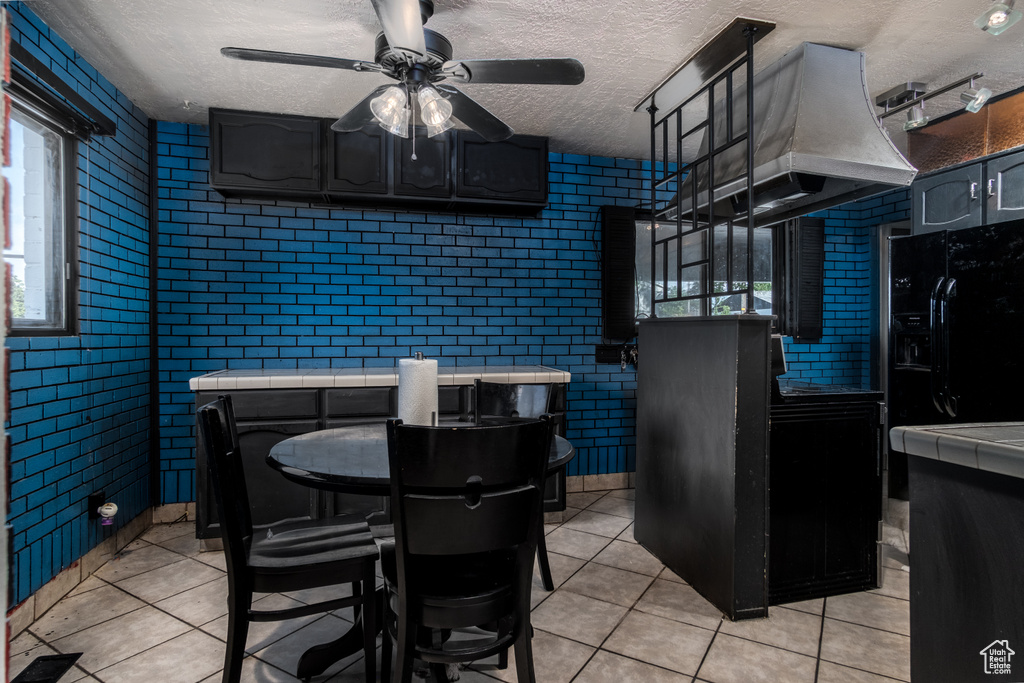 Dining area featuring light tile patterned floors, a ceiling fan, a textured ceiling, and brick wall